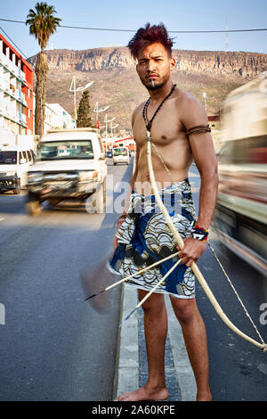 Tribal Mann mit seinem traditionellen Bogen und Pfeile in der Mitte der Stadt mit Autos vorbei, Lubango, Angola Stockfoto