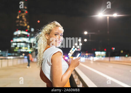 Junge Frau in London bei Nacht und mit ihrem Smartphone Stockfoto