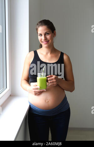 Junge schwangere Frau trinkt frischen und gesunden grünen Smoothie Stockfoto