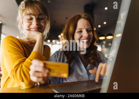 Zwei glückliche weibliche Freunde mit Laptop und Kreditkarte in einem Cafe Stockfoto