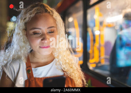Junge Frau in London bei Nacht an Ihrem Smartphone suchen, Bus im Hintergrund Stockfoto