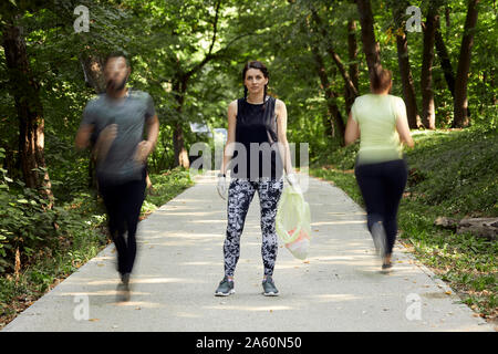 Leute und junge Frau plogging auf Waldweg Stockfoto