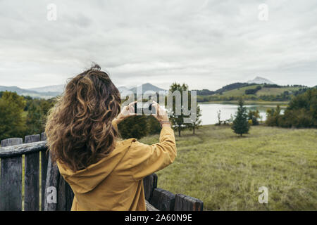 Junge Frau tragen gelbe Fell ein Foto mit Ihrem Smartphone Stockfoto