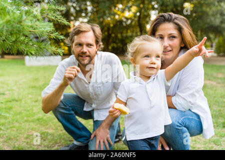 Eltern mit kleinen Tochter zeigen mit dem Finger auf einer Wiese Stockfoto