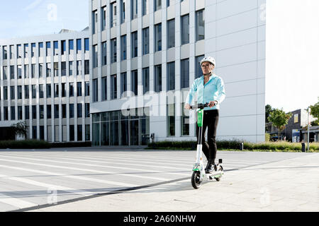 Reife Frau reiten Elektroroller in der Stadt Stockfoto