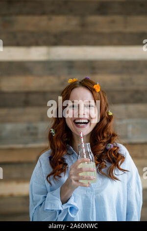 Portrait von Lachende rothaarige Frau mit Blüten im Haar trinken Limonade Stockfoto