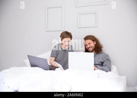 Junges Paar mit Laptop im Bett zu Hause. Stockfoto