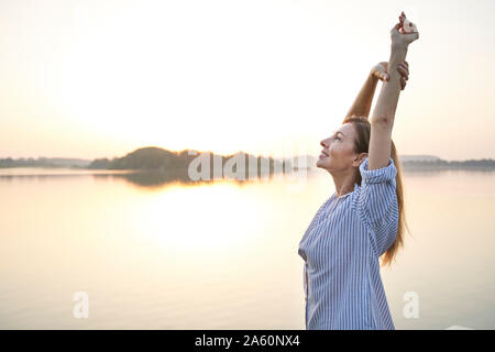 Gerne reife Frau stretching an einem See bei Sonnenaufgang Stockfoto