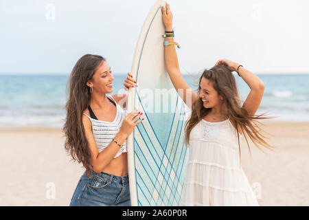 Zwei glückliche weibliche Freunde mit Surfbrett am Strand Stockfoto