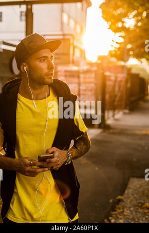 Portrait von tätowierten jungen Mann Musik hören mit Kopfhörern und Smartphone bei Sonnenuntergang Stockfoto