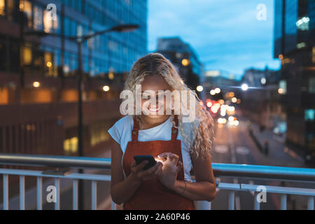 Junge Frau in die Stadt in der Dämmerung an Ihr Smartphone Stockfoto