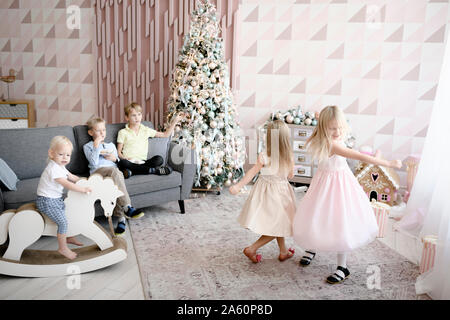 Zwei Mädchen tanzen im Wohnzimmer, während die Jungen ansehen Stockfoto