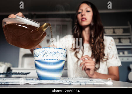 Junge Frau Gießen Tee in Tasse Stockfoto