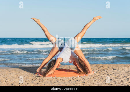 Zwei Frauen praticing Acro Yoga am Strand, in den nach unten schauenden Hund Position Stockfoto