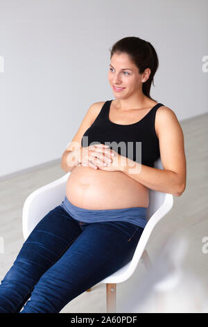 Junge schwangere Frau sitzt auf einem Stuhl und denkt an die Zukunft Stockfoto