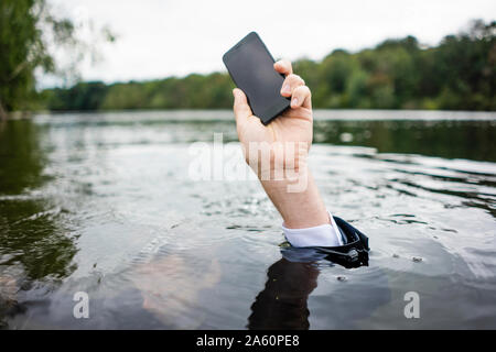 Der Geschäftsmann hand Handy in einem See Stockfoto