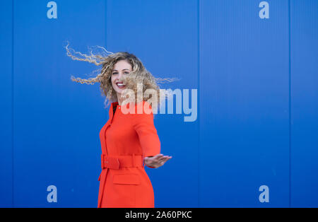 Portrait von glücklichen jungen Frau das Tragen der roten Kleid vor blauem Hintergrund Stockfoto