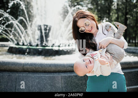 Mutter spielt mit ihrem Baby in der Nähe von einem Brunnen Stockfoto