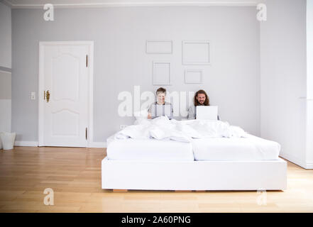 Junges Paar mit Laptops im Bett zu Hause. Stockfoto
