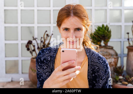 Portrait von lächelnden rothaarige junge Frau mit Handy auf der Terrasse Stockfoto