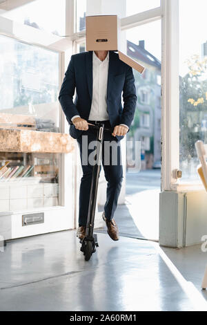 Geschäftsmann mit Karton auf dem Kopf, Reiten e-Scooter in einem Coffee Shop Stockfoto