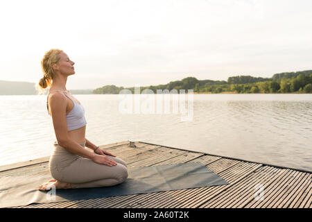 Junge Frau mit Yoga auf einem Steg am See Stockfoto