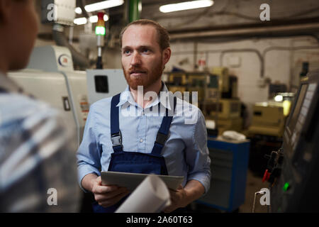 Junge Unternehmer mit Tablet PC-Arbeit tragen und im Gespräch mit seinem Kollegen bei der Arbeit in der Fabrik Stockfoto