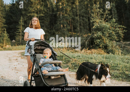 Mutter mit Baby im Kinderwagen und Hund zu Fuß auf den Waldweg Stockfoto