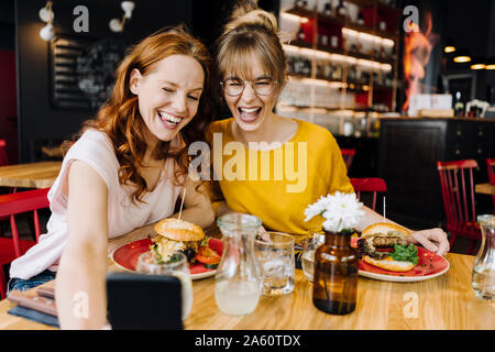 Zwei glückliche weibliche Freunde Burger in und unter einem selfie in einem Restaurant Stockfoto