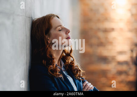 Redheaded Geschäftsfrau mit einer Unterbrechung gegen eine Wand gelehnt im Amt. Stockfoto