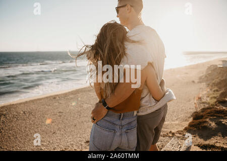 Liebevolle junge Paar genießt die Aussicht auf den Strand bei Sonnenuntergang Stockfoto