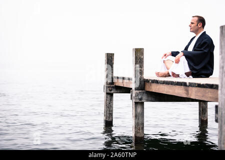 Mann sitzt auf Steg Yoga Übung, Starnberger See, Deutschland Stockfoto