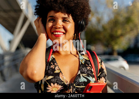 Weibliche afroamerikanischen mit Kopfhörern und Smartphone Musik hören, seitlich auf der Suche Stockfoto