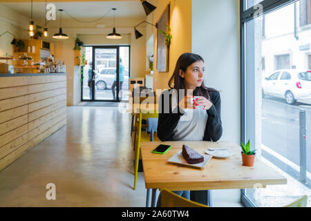 Junge Frau sitzt in einem Cafe Blick aus Fenster Stockfoto