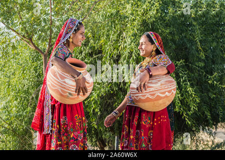 Zwei Ahir Frauen in traditionelle bunte Kleidung tragen von Wasser in einem Ton Kanne, tolle Rann von Kutch Wüste, Gujarat, Indien, Asien Stockfoto