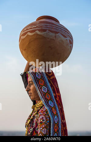 Ahir Frau in traditionelle bunte Tuch mit Wasser in einem Ton Krug auf dem Kopf, große Rann von Kutch Wüste, Gujarat, Indien, Asien Stockfoto