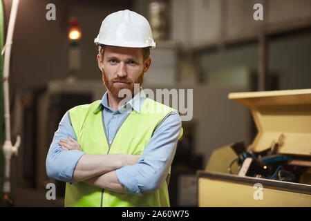 Portrait von zuversichtlich bärtigen Vorarbeiter in der schützende Arbeitskleidung Stehen mit verschränkten Armen und Kamera in der Anlage Stockfoto