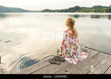 Junge Frau sitzt auf einem Steg am See Stockfoto