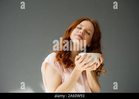 Portrait von entspannter rothaarige Frau mit Müsli Schüssel gegen grauer Hintergrund Stockfoto