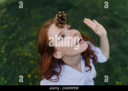 Rothaarige Frau balancing a Pine Cone auf ihrer Stirn Stockfoto