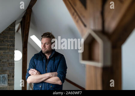 Architekt stand mit verschränkten Armen vor Ort gekreuzt, mit Haus Form Übergabe auf Holz von einem Dachstuhl Stockfoto