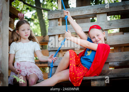 Mädchen verkleidet als Prinzessin und superwoman Spielen in einem Baumhaus Stockfoto