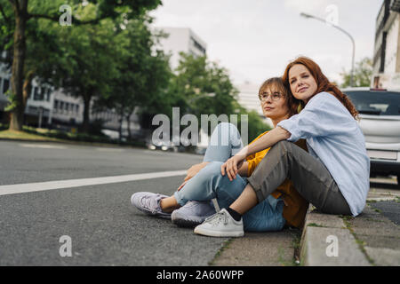 Weibliche Freunde am Straßenrand sitzen in der Stadt Stockfoto