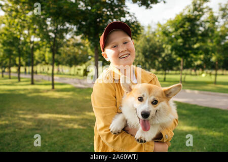 Lächelnde Junge hielt seine Welsh Corgi Pembroke in einem Park Stockfoto