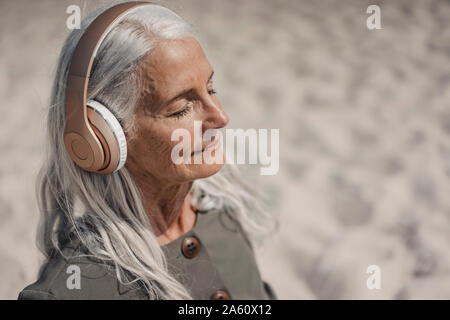 Ältere Frau Musik hören mit Kopfhörern am Strand Stockfoto