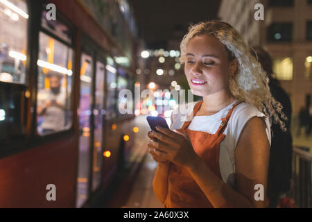 Junge Frau in London bei Nacht an Ihrem Smartphone suchen, Bus im Hintergrund Stockfoto