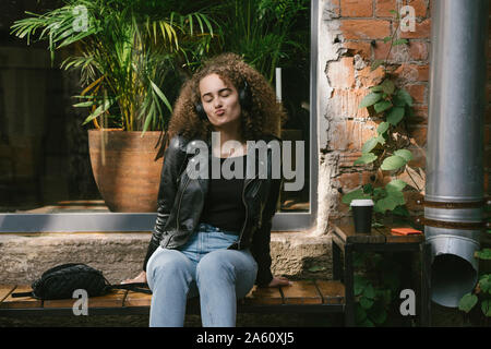 Portrait von teenage Mädchen an Outdoor Cafe Musik hören mit Kopfhörern sitzen und Smartphone Stockfoto