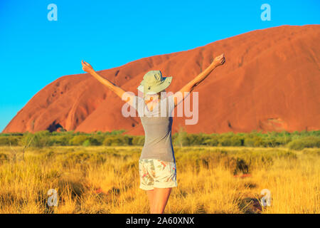 Sorglos touristische Frau mit erhobenen Armen genießt Uluru (Ayers Rock) bei Sonnenuntergang im Uluru-Kata Tjuta National Park, UNESCO, Northern Territory, Australien Stockfoto