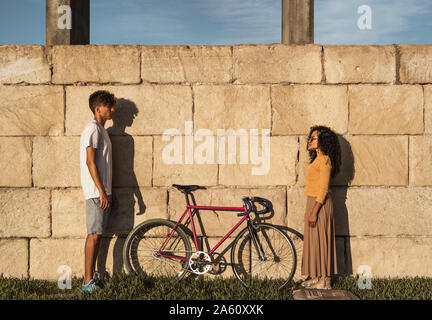Junges Paar mit dem Fahrrad, vor der Wand stehend, von Angesicht zu Angesicht Stockfoto