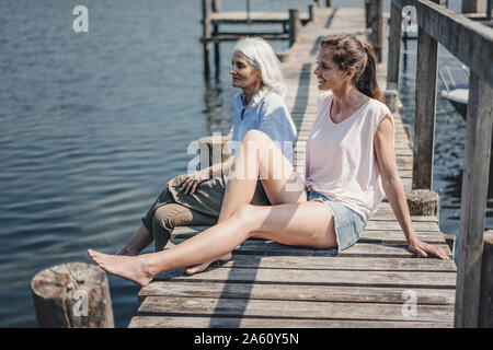 Mutter und Tochter sitzen am Bootsanleger, Entspannen am Meer Stockfoto